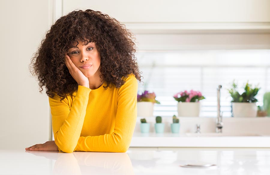 african american woman wearing a yellow sweater and long curly beautiful hair in the kitchen looking tired and bored with depression problems with crossed arms.
